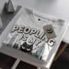 peopling-is-my-cardio-black-scowl-folded-tshirt-tag Folded white t-shirt showing the 'Peopling is my Cardio' graphic and Black Scowl brand tag.