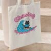 Woman carrying a Black Scowl tote bag on her shoulder with a funny surfing cat design, perfect for a sarcastic beach look.