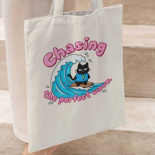 Woman carrying a Black Scowl tote bag on her shoulder with a funny surfing cat design, perfect for a sarcastic beach look.