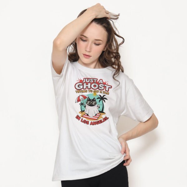 Model wearing the Just A Ghost Trying To Get A Tan In Los Angeles t-shirt in a sunny outdoor setting. Sarcastic summer streetwear.