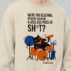 Close-up view of the Black Scowl graphic apparel on a cream sweatshirt. The edgy streetwear print displays an existential black cat drummer and dark humor typography.
