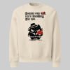 Flat front product shot of the Black Scowl dark humor streetwear sweatshirt in beige, presenting the full cynical cat graphic and clean modern fashion silhouette.