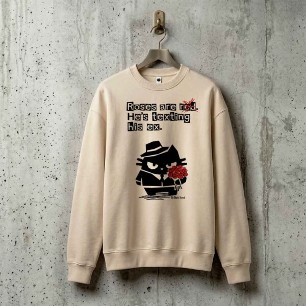 Premium heavyweight Black Scowl streetwear sweatshirt hanging on a concrete wall, displaying a funny anti-valentine cat design and sarcastic text.