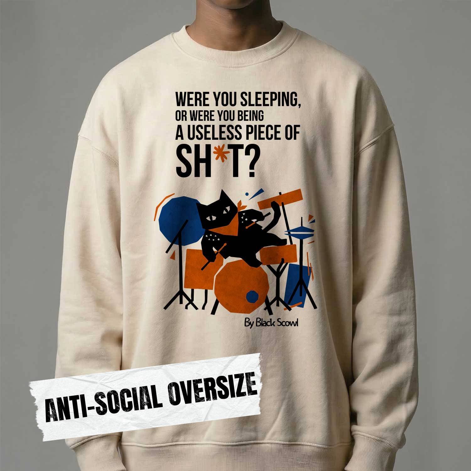 Male model wearing Black Scowl heavyweight oversize sweatshirt with a sarcastic dark humor quote about being useless and a cynical drummer cat graphic.