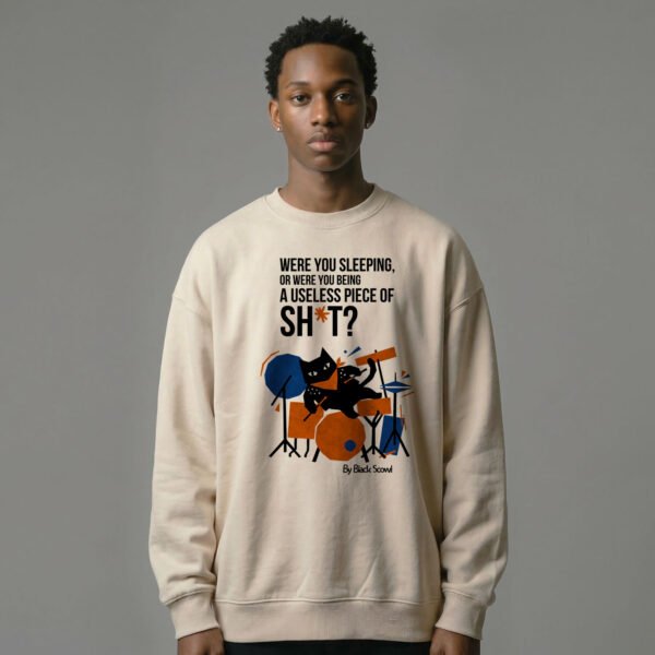 Male model wearing Black Scowl heavyweight oversize sweatshirt with a sarcastic dark humor quote about being useless and a cynical drummer cat graphic.