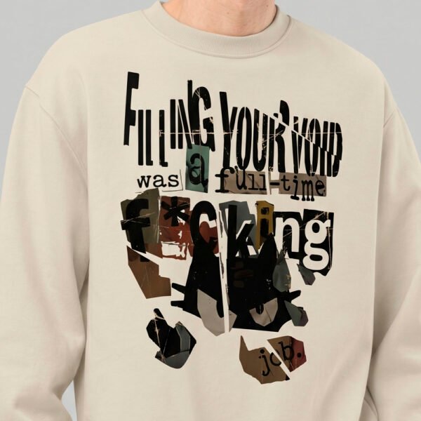 Close-up detail of the Black Scowl beige sweatshirt, showcasing the modern graphic wear print with a dark cat and ransom-note style lettering.