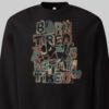 Close-up detail of the Black Scowl "Born Tired Stay Tired" print on a black sweatshirt, highlighting the grunge urban clothing aesthetic with a sarcastic cat and retro gamer motifs.