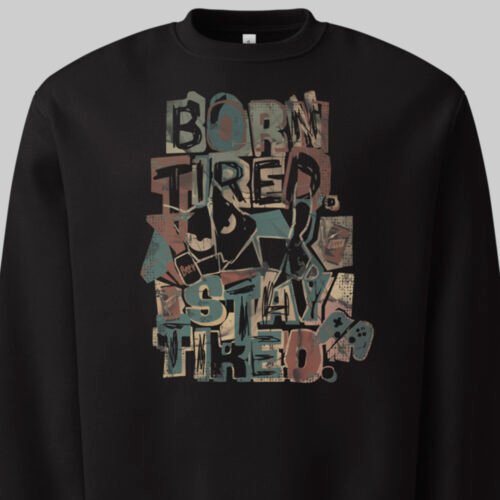 Close-up detail of the Black Scowl "Born Tired Stay Tired" print on a black sweatshirt, highlighting the grunge urban clothing aesthetic with a sarcastic cat and retro gamer motifs.