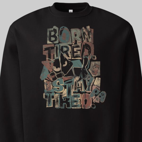 Close-up detail of the Black Scowl "Born Tired Stay Tired" print on a black sweatshirt, highlighting the grunge urban clothing aesthetic with a sarcastic cat and retro gamer motifs.