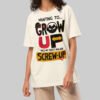 A female model wearing the Black Scowl cream heavyweight graphic tee with a cynical urban design and a relaxed, drop-shoulder avant-garde fit.