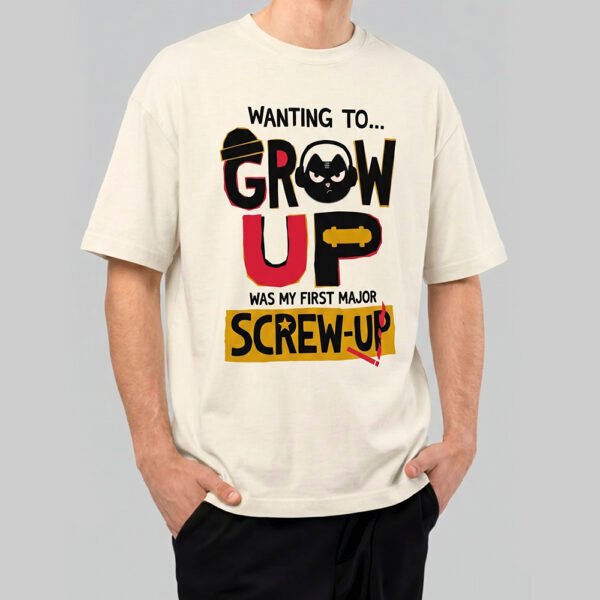 Front view of a male model wearing a Black Scowl cream heavyweight t-shirt featuring a sarcastic "Wanting To Grow Up Was My First Major Screw-Up" graphic with a grumpy cat icon.