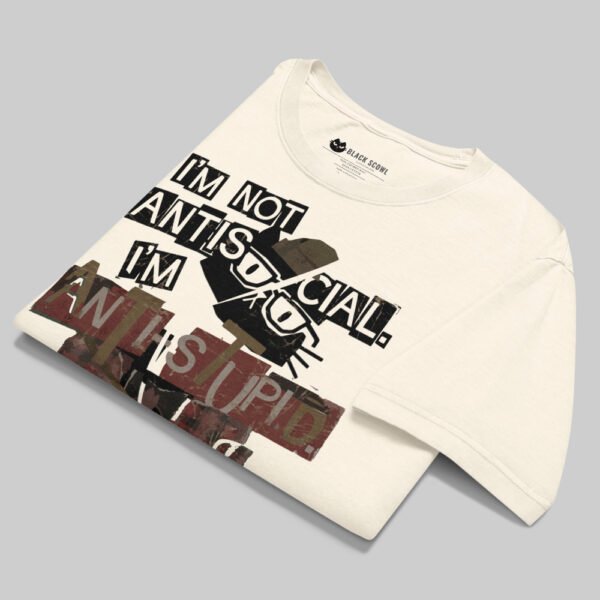 A professionally folded Black Scowl cream graphic tee on a gray background, showcasing the premium heavyweight cotton and bold artistic print