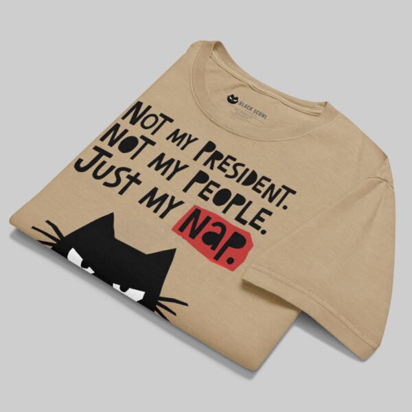 A professionally folded Black Scowl sand graphic tee on a gray background, showcasing the bold typography and artistic streetwear design.