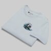 Professional flat-lay shot of a folded Black Scowl light blue oversized graphic tee, highlighting the premium structured cotton and surfing cat chest print.