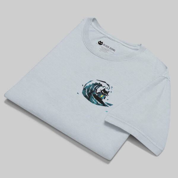 Professional flat-lay shot of a folded Black Scowl light blue oversized graphic tee, highlighting the premium structured cotton and surfing cat chest print.