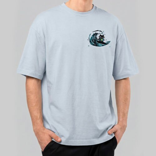 Front view of a male model wearing a Black Scowl light blue oversized t-shirt featuring a small graphic of a cynical black cat surfing on a wave.