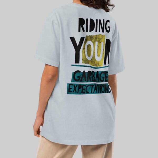 A female model showcasing the back of a Black Scowl light blue streetwear t-shirt with a large "Garbage Expectations" graphic and a relaxed, oversized fit.