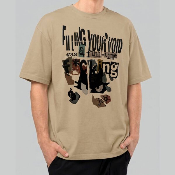 Front view of a male model wearing a Black Scowl sand-colored heavyweight t-shirt featuring a cynical "Filling Your Void" collage-style graphic with a black cat.