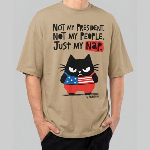 Front view of a male model wearing a Black Scowl sand-colored oversized t-shirt featuring a cynical "Just My Nap" political satire graphic with a black cat.
