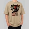 Front view of a male model wearing a Black Scowl sand-colored oversized t-shirt featuring a cynical "Punk Drunk Single Mom" graphic with a cat illustration.