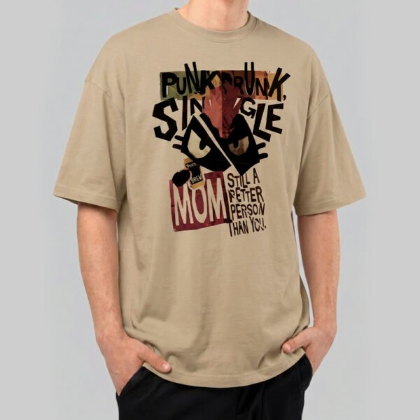 Front view of a male model wearing a Black Scowl sand-colored oversized t-shirt featuring a cynical "Punk Drunk Single Mom" graphic with a cat illustration.