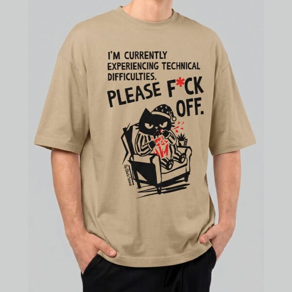 Front view of a male model wearing a Black Scowl sand oversized t-shirt featuring a sarcastic "Technical Difficulties" graphic with a cat in pajamas eating popcorn.