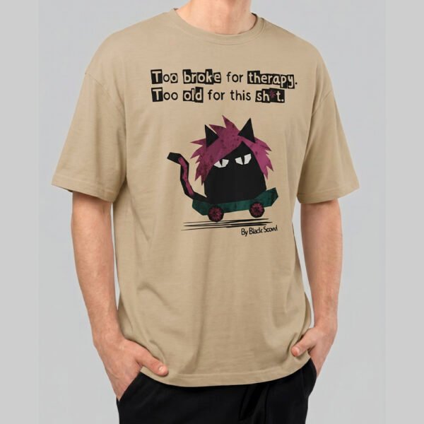 Front view of a male model wearing a Black Scowl sand oversized t-shirt with a sarcastic cat on a skateboard graphic and "Too broke for therapy" text.