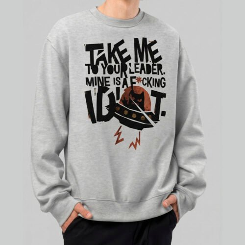 A man wearing a Black Scowl grey streetwear sweatshirt featuring a cynical cat in a UFO with the text Take Me To Your Leader Mine Is A Fool.