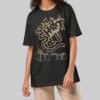 A female model wearing the Black Scowl black heavyweight graphic tee with a modern oversized fit and avant-garde aesthetic.